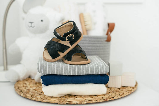 Black leather baby sandals resting on a stack of folded blankets in a woven basket - Babe Basics